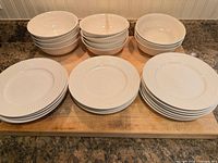 Dinnerware set stacked on cutting board: three stacks of bowls, three stacks of plates