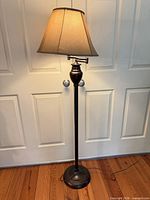 Full view of lit floor lamp showing bronze base and beige shade