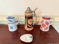 Front view of blue floral pitcher, German beer stein with pewter lid, red pitcher (not part of lot) and Coalport trinket egg