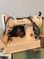 Left side view of Singer sewing machine inside open green case showing badge, motor and cords