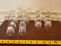 Fourteen inverted Waterford cordial glasses on table with measuring tape for scale