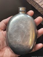 Front view of oval metal flask held in hand