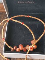 Necklace in box showing overall design with tan beads, red spacers and carnelian front section