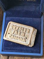 Front of cast bronze tag showing raised lettering and mounting holes