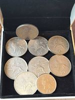 Open presentation box with nine large U.K. 10 pence coins, one propped for obverse view
