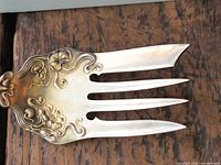 Blade of fork showing gold gilt, pierced design, three tines, floral scrolls.