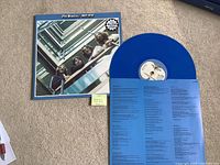 Front cover of gatefold sleeve with one blue vinyl record partially removed