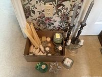 overview of box with multiple candles and holders plus pair tall metal candlesticks