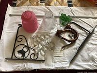 All items laid out on cloth: two glass shades, chandelier prisms, wooden holdback, iron brackets, metal rod, glass of green marbles