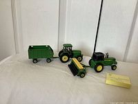 Four John Deere metal toy pieces: two tractors and two implements