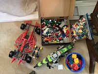Overview of lot: red K'NEX vehicle, box of bricks, zip bag of bricks, green spacecraft, blue tub of Zaks