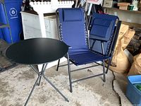 Open blue zero gravity chair with headrest and round black metal folding table visible