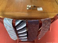 Four ties draped over chair, cufflinks and tie bars on table