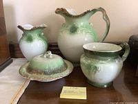 Front view of four green and white semi-porcelain bathroom pieces on table