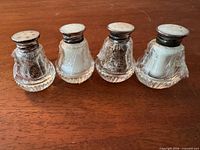 Four crystal shakers side by side showing bodies and sterling lids wrapped in protective film