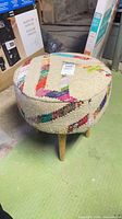 Round woven ottoman showing multicolour patterned fabric and wooden legs
