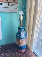 Full view of lamp showing pottery base, wood neck, harp, bulb, and power cord