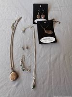 All jewelry pieces laid out: locket necklace, green stone pendant set, cutlery necklace and earrings, stud earrings