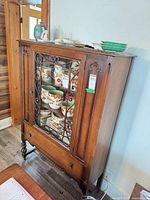 Full view of cabinet showing wood finish, glass door with scrollwork, overall style and size