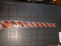 Full view of sealed necktie showing black fabric with red diagonal stripes and yellow AC/DC logo