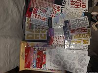Assorted sticker sheets spread out showing glitter letters, numbers, hearts and rhinestone strips