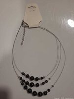 Full view of necklace on display card showing three-strand design and attached stud earrings