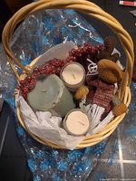 Top view of wicker basket showing green pillar candle, two ivory votive candles in glass, red bead berry garland and plush reindeer