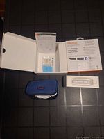 Open box showing manual, lancets/test strips, blue case, lancing device