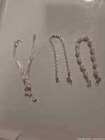 Three bracelets laid out: multi-strand charm, rope chain, linked panel