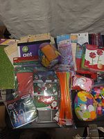 Overall lot showing unopened craft supplies including paper pads, foam sheets, stick jar, pipe cleaners, stickers, beads, pom-poms