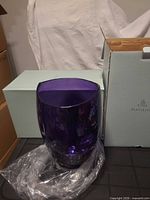 Purple glass hurricane vase in front of PartyLite box