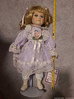 Full view of 18-inch porcelain doll on stand with tape measure for scale and certificate tag visible
