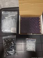 Open box with grid of purple glass vials plus three zip bags containing droppers, caps and stoppers