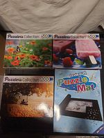 Front view of four boxed items: three Puzzler's Collection jigsaw puzzles (500-piece butterfly flowers, 500-piece fruit popsicle, 1000-piece beach swing) and LaVieVert Puzzle Mat kit