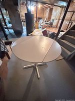 Table viewed from side with one leaf extended, showing pedestal base and surrounding area