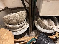 Stacked exposed-aggregate concrete bowl planters and scalloped urn tops in storage