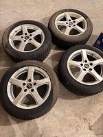 Four silver alloy wheels with tires arranged on floor