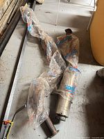 Full view of exhaust system components on floor with protective wrap