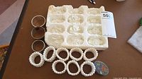 Styrofoam tray holding 12 white porcelain roses, 3 silverplate napkin rings, 8 pearl napkin rings