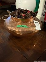 Bulbous hammered copper pot with handles and pinecone filler on wooden floor