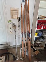 Full view of both pairs of wooden skis standing next to two pairs of silver poles, boots not in frame