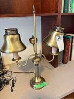 Two-light brass-tone table lamp with metal shades on desk