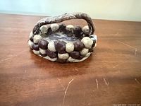 Side view of handmade ceramic basket showing brown/beige glazed coil walls and handle