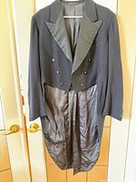 Front view of black wool tailcoat showing double-breasted front, satin peaked lapels, full tails and striped satin lining