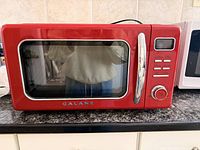 Front view of red Galanz retro microwave on countertop showing door, handle, controls and brand logo