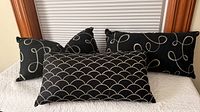 Three black pillows with contrasting white patterns displayed on bed