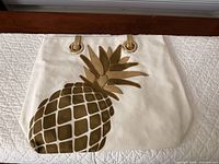 Front view of white cotton tote bag displaying pineapple applique and handles
