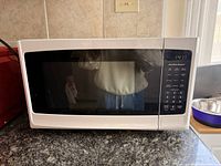 Front view of white Hamilton Beach microwave showing door, control panel, and LED display