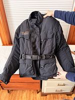 Front of black Gericke Dri-Tech jacket with belt, pockets, high collar
