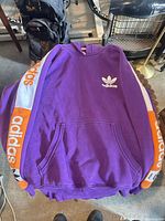 Front view showing purple hoodie, Trefoil logo, kangaroo pocket, sleeve branding